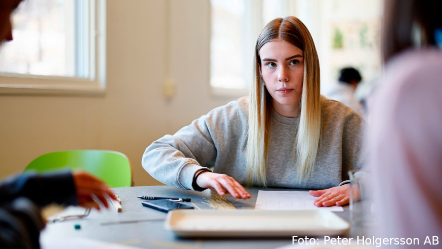 Elev med papper och pennor sitter vid en bänk.